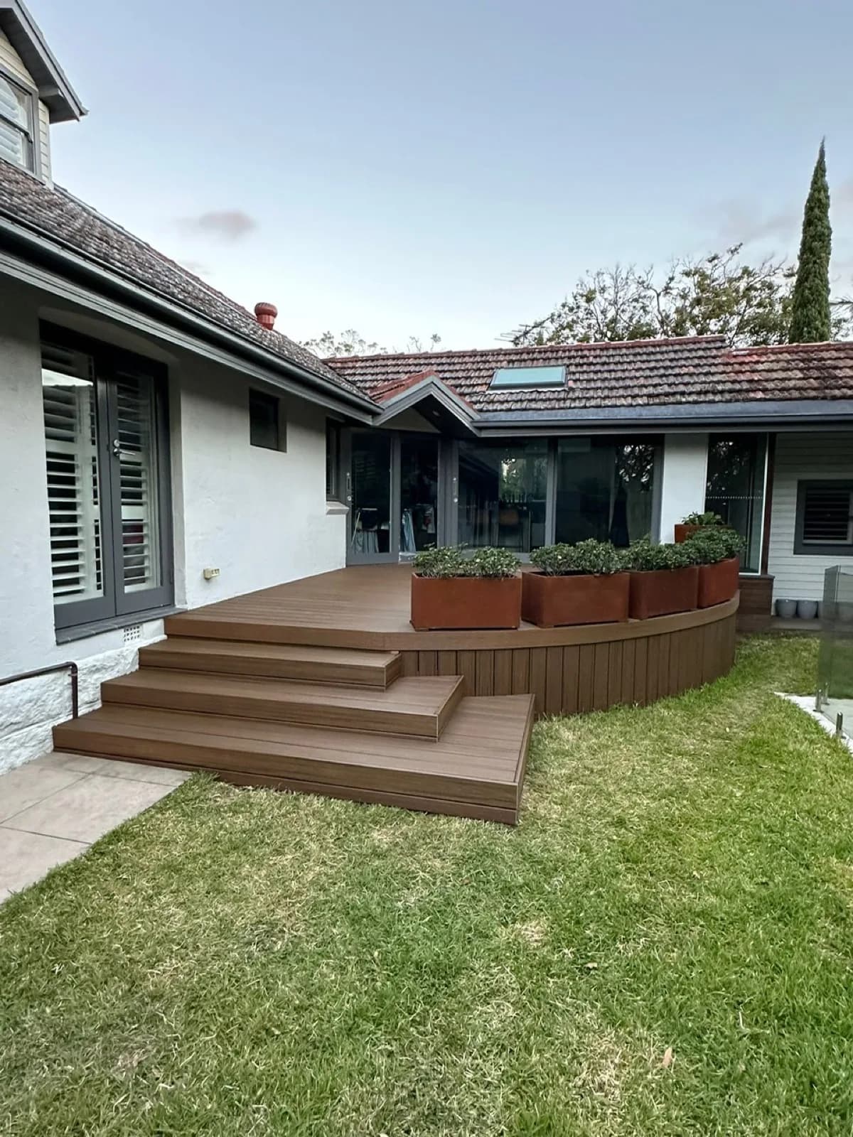 Curved brown composite deck with wide multi-tread steps and corten planter boxes on lawn