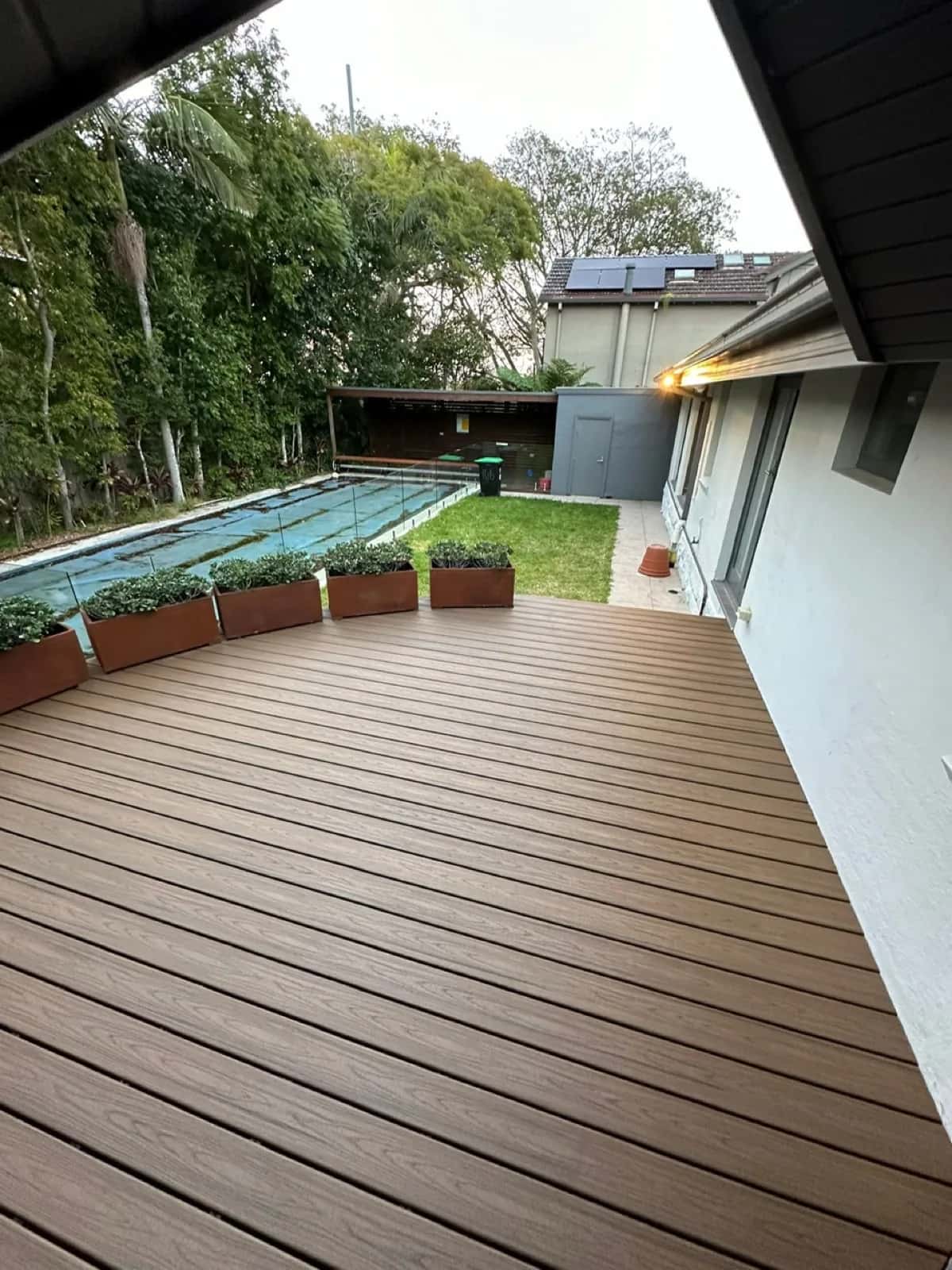 Deck surface towards pool with glass pool fence, planters on curved edge