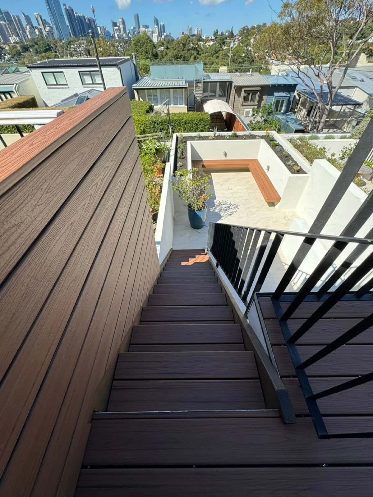 External stair clad in composite with black balustrade, looking down to terrace bench, city skyline