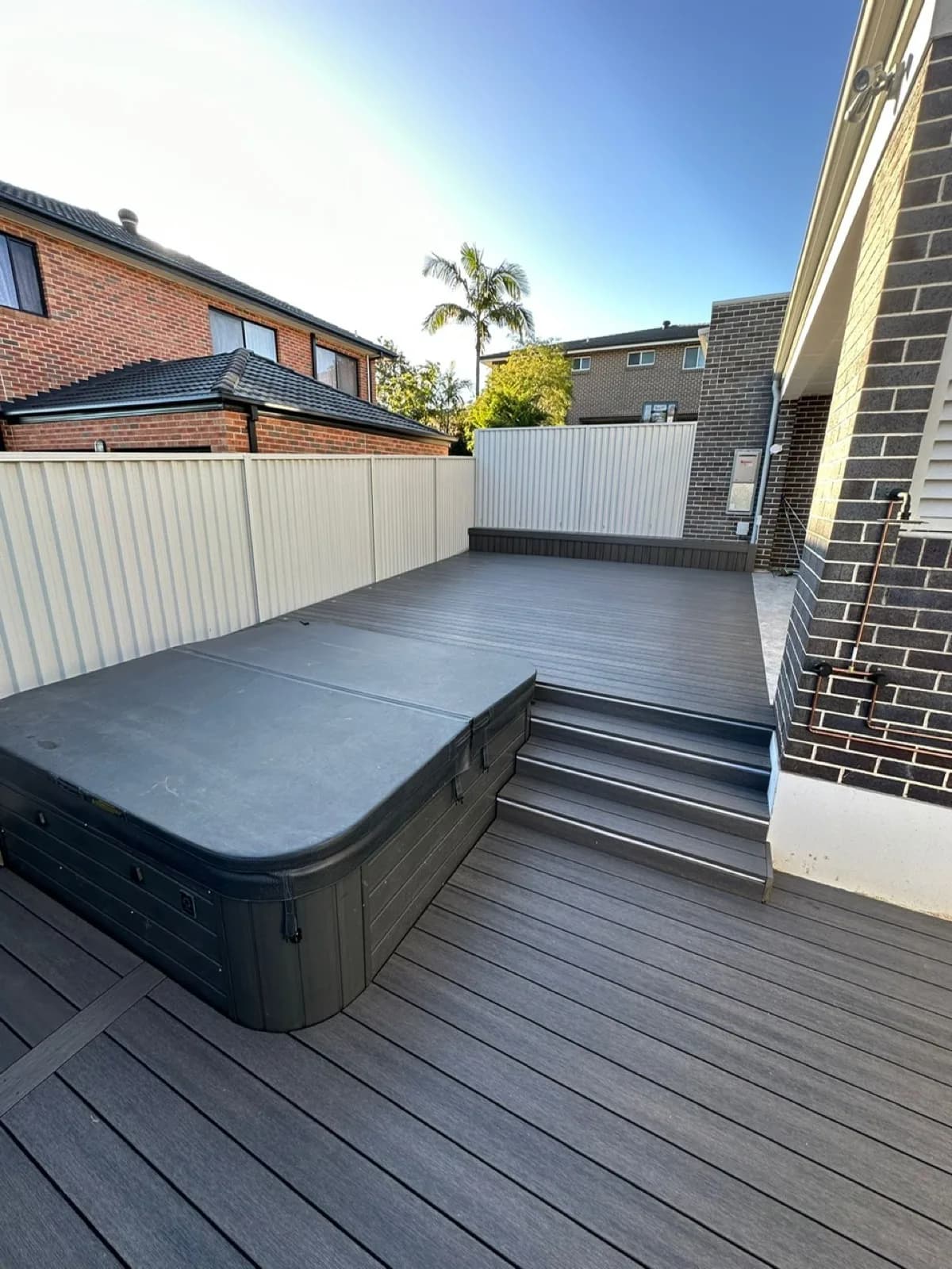 Grey composite deck with in-ground spa set into deck, steps to house