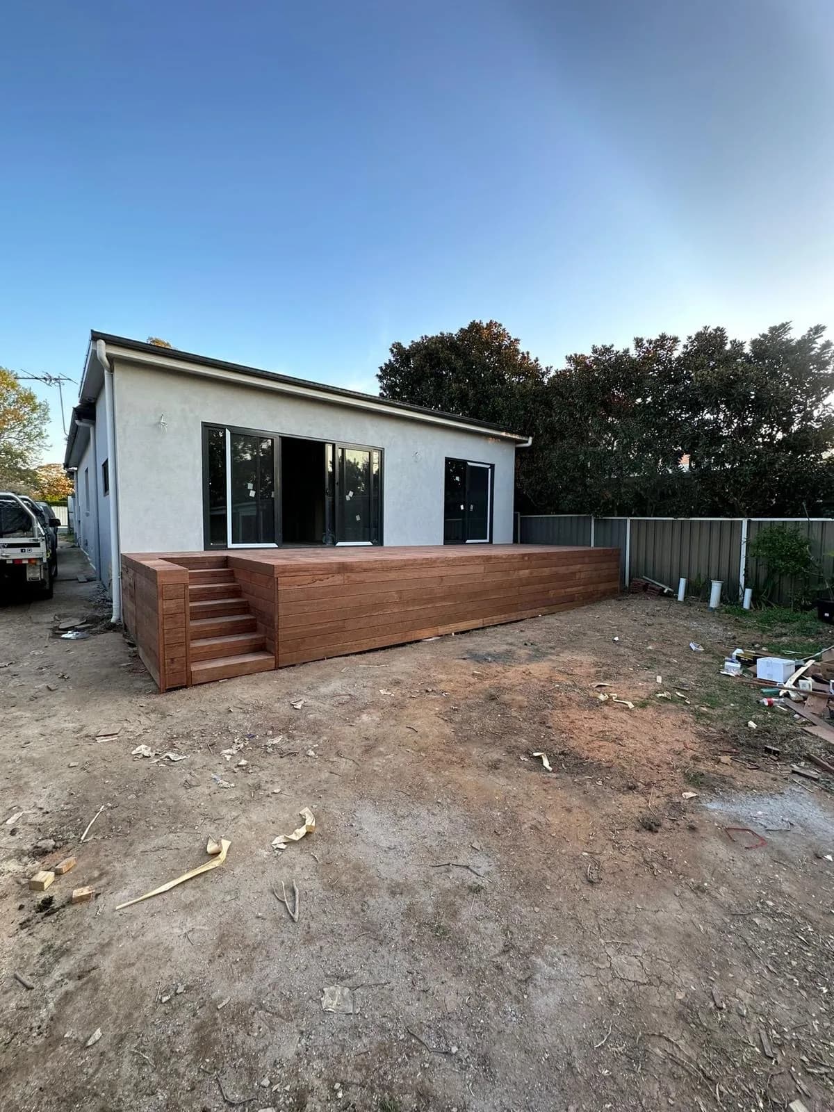 New raised merbau deck across rear of rendered house with boxed stair, bare dirt yard