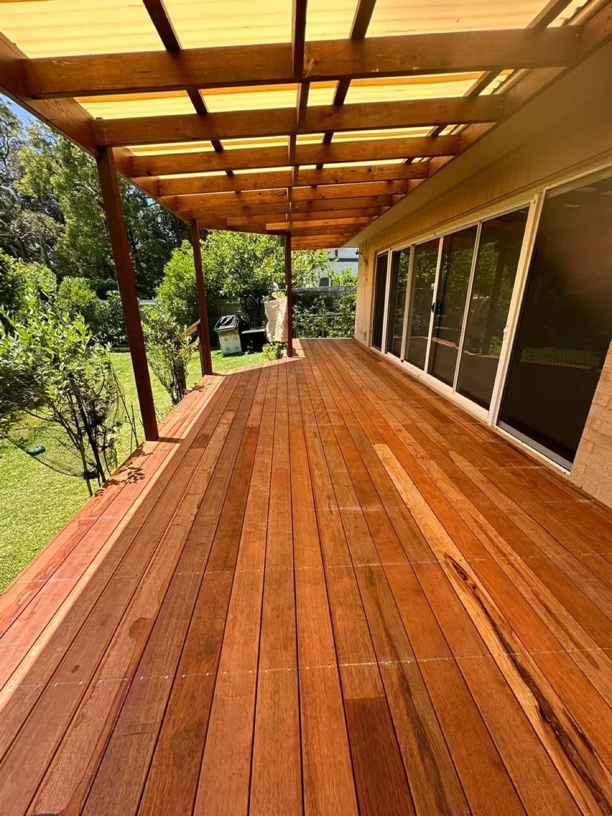 Long merbau deck under timber pergola with translucent roofing, sliding doors