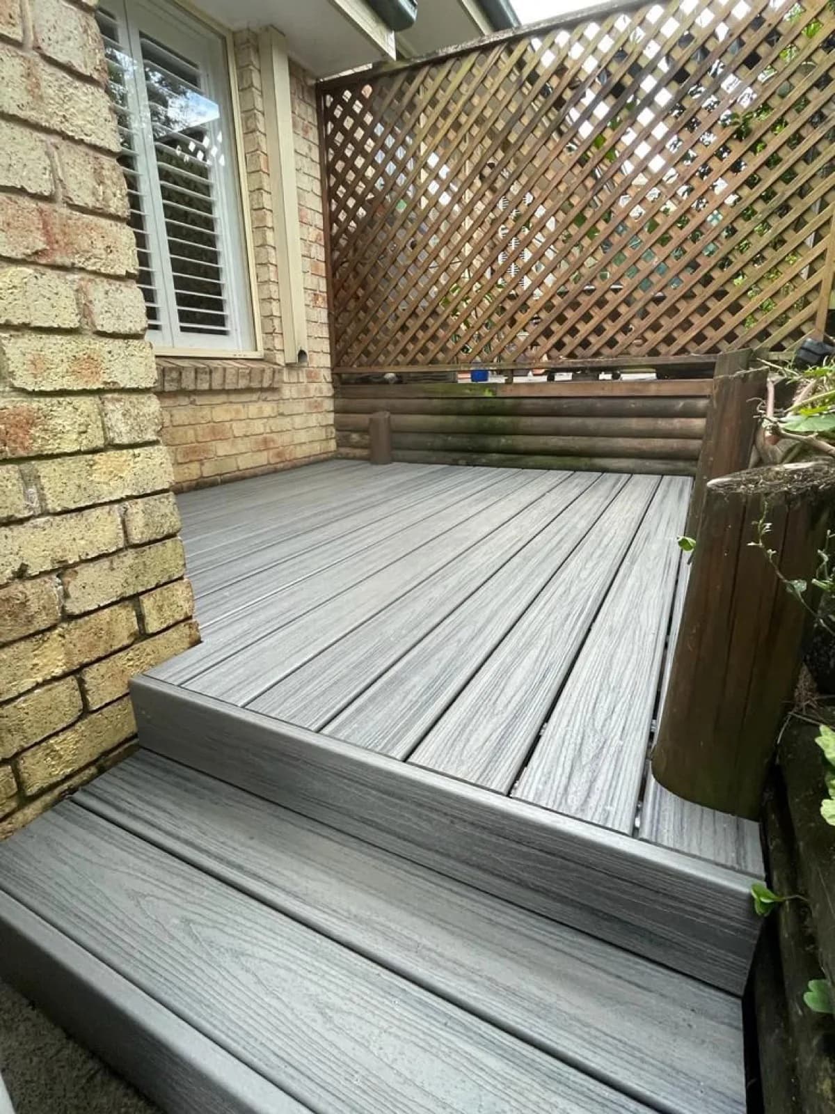 Grey composite deck with step beside lattice screen and brick wall