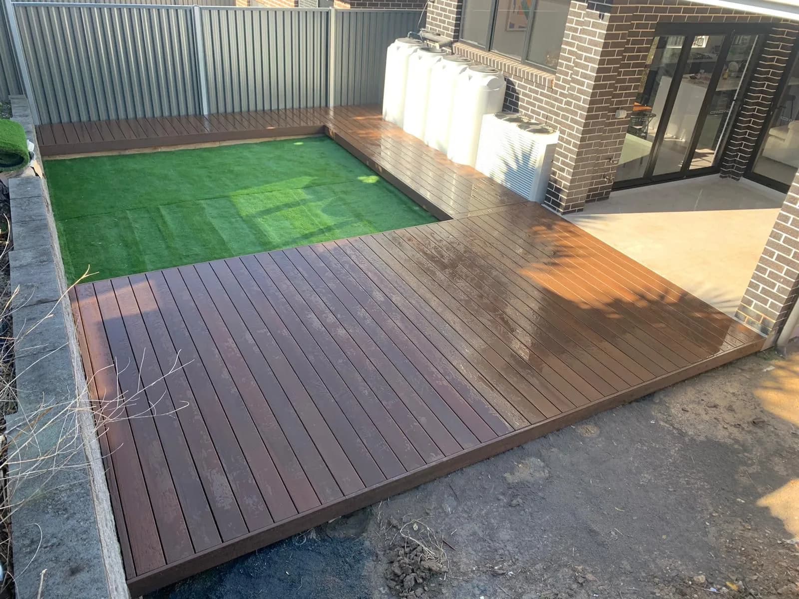 Dark brown composite deck in L around artificial turf, new-build backyard